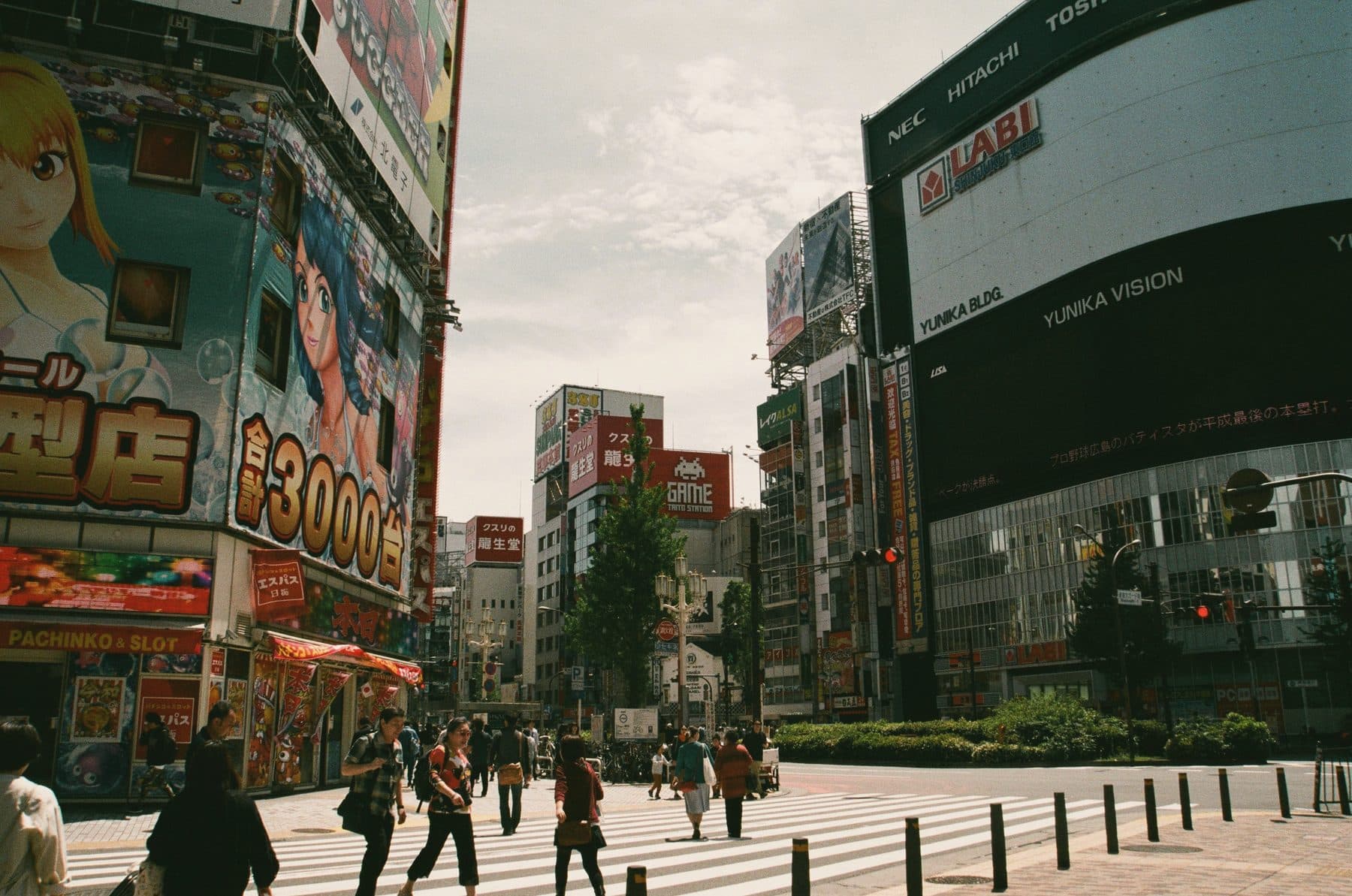 People crossing a street by the giant screens of Shinjuku, Tokyo, on a sunny day