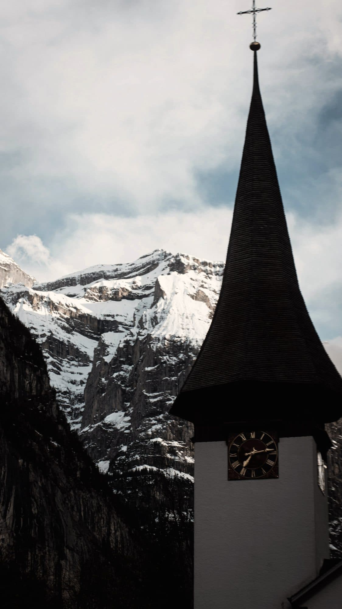 A dark-spired village church beneath snow-covered Swiss peaks
