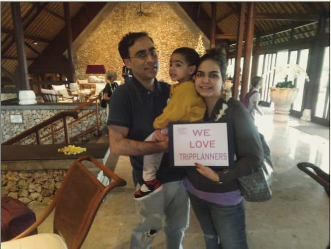 A family holding a We love Tripplanners sign at their hotel