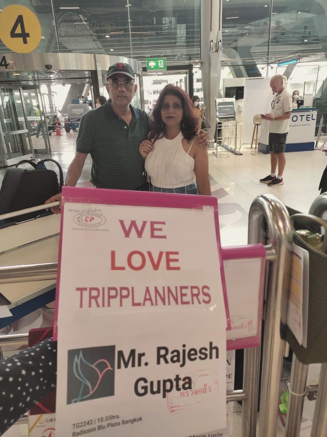 A couple at the airport beside a We love Tripplanners welcome board