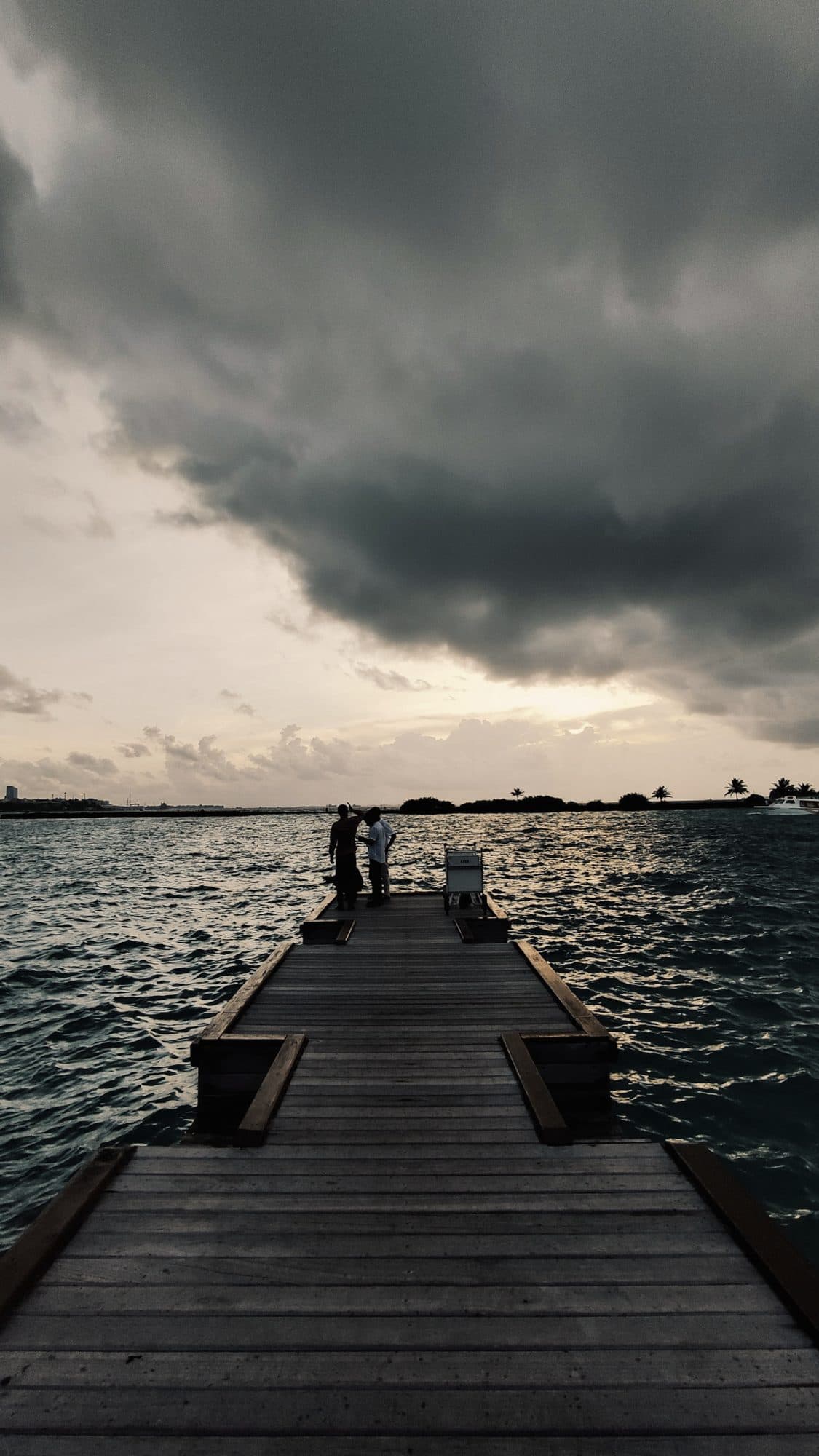 A wooden jetty running out into a dark sea under storm clouds